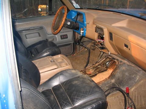 1987 Ford Bronco - The interior of the truck shows signs of wear and tear, with exposed wires and a dirty floor.