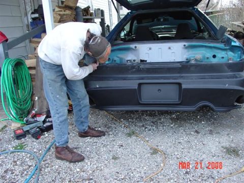 1993 Ford Probe - A person works on the rear bumper of a teal car, with the trunk open.