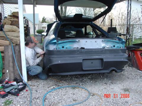 1993 Ford Probe - A man works on the rear bumper of a teal 1993 Ford Probe with its trunk open.