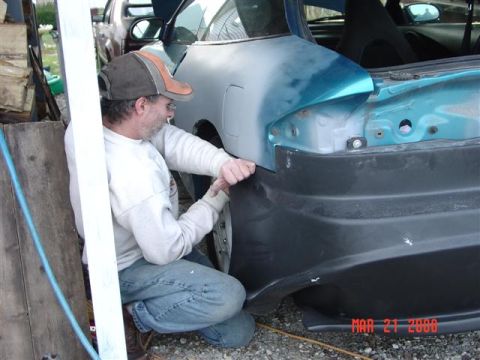 1993 Ford Probe - Man works on attaching a rear bumper to a car, with another vehicle in the background.