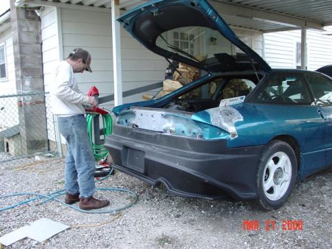 1993 Ford Probe - A person uses a grinder on the rear bumper of a teal coupe with its hood and trunk open.