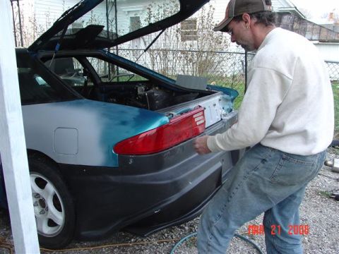 1993 Ford Probe - A man is seen working on the rear bumper of a car, with the trunk open, revealing the interior.