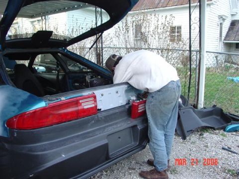 1993 Ford Probe - A person is working on the rear of a car, with the trunk open and some parts disassembled.