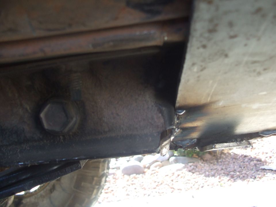 Underbody view of a black frame rail and body mount bolt above a gravel driveway