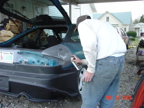 1993 Ford Probe - A person works on the body of a car, applying spray paint to the rear quarter panel. An Indiana license plate is visible on the trunk area…