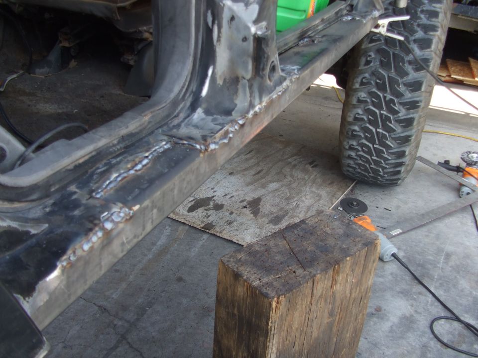 Freshly welded steel rocker plate on a vehicle body with angle grinders on the floor