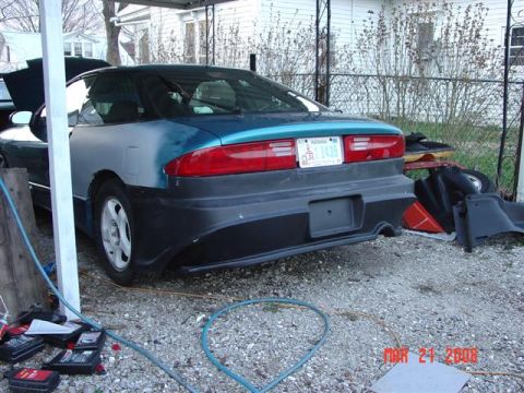1993 Ford Probe - The rear of a 1993 Ford Probe is shown, with one rear quarter panel appearing to be in primer. Parts are visible to the right.