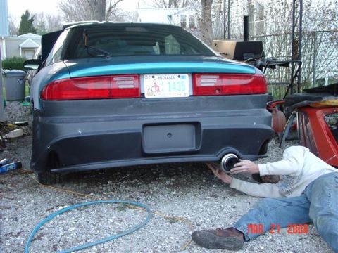 1993 Ford Probe - A person works on the exhaust pipe of a teal car's rear bumper.