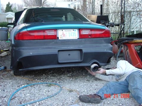 1993 Ford Probe - Man works on the exhaust system of a 1993 Ford Probe in a gravel driveway.