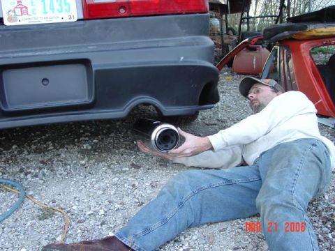 1993 Ford Probe - A man works on the exhaust system of a car, with other vehicle parts visible in the background.