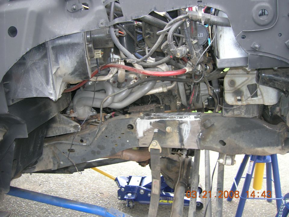 close-up of vehicle engine and frame with exhaust headers visible, vehicle is on jack stands