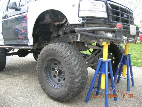 1996 Ford Bronco - A modified Ford Bronco is shown with its front end elevated on jack stands, revealing its lifted suspension and large tires.