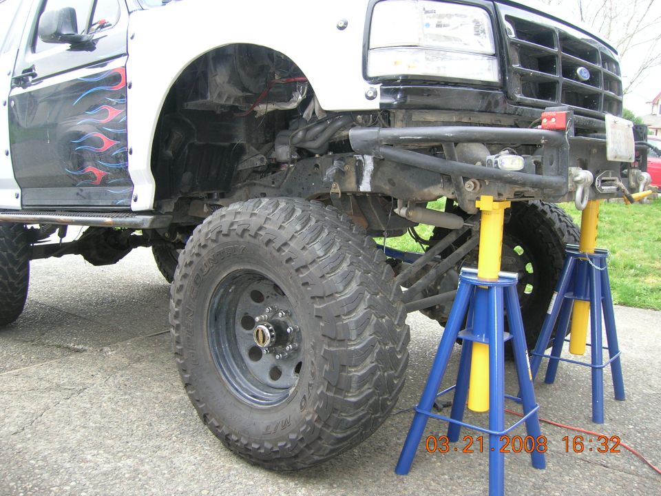 Modified Ford Bronco with flame decals on the side, lifted suspension, and large off-road tires, supported by jack stands