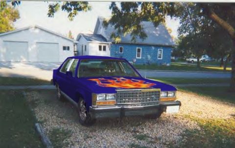 1987 Ford Crown Victoria LTD - A blue sedan with flame decals is parked in front of a house and garage on a sunny day.