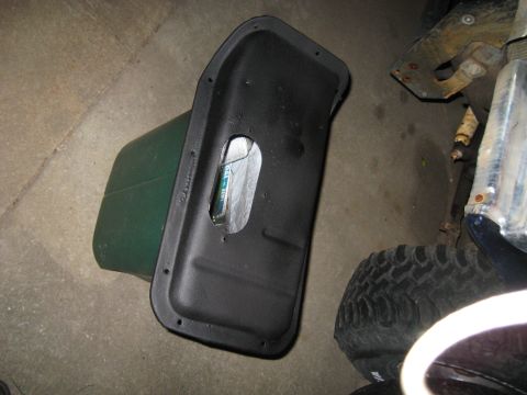 1978 Ford Bronco - A black plastic panel with a hole in it is shown on the ground next to a green gas can and a vehicle tire.