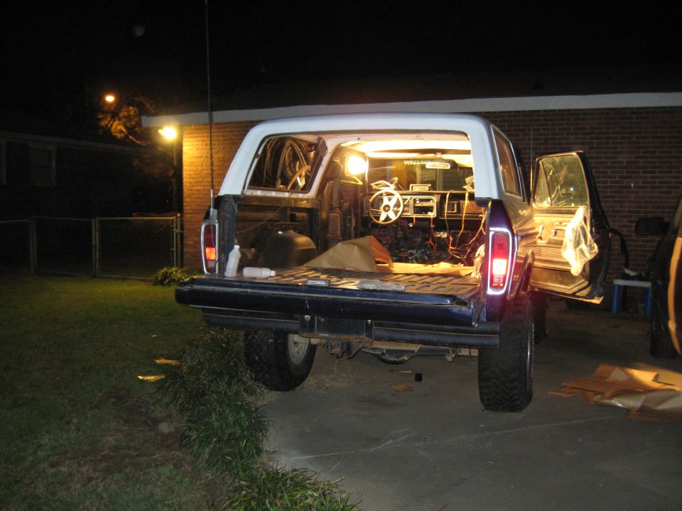 1978 Ford Bronco with open tailgate and doors, interior lights on, parked in driveway at night