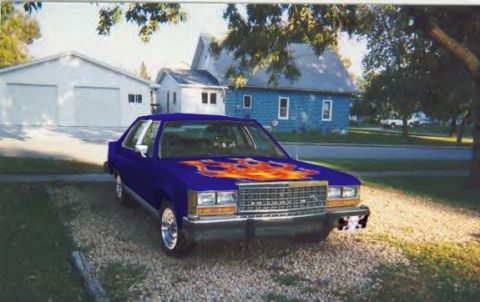 1987 Ford Crown Victoria LTD - A blue sedan with flame decals on the hood is parked in front of a house and garage.