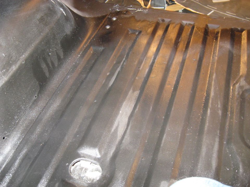Black ribbed vehicle floor with some rust spots and a circular cutout