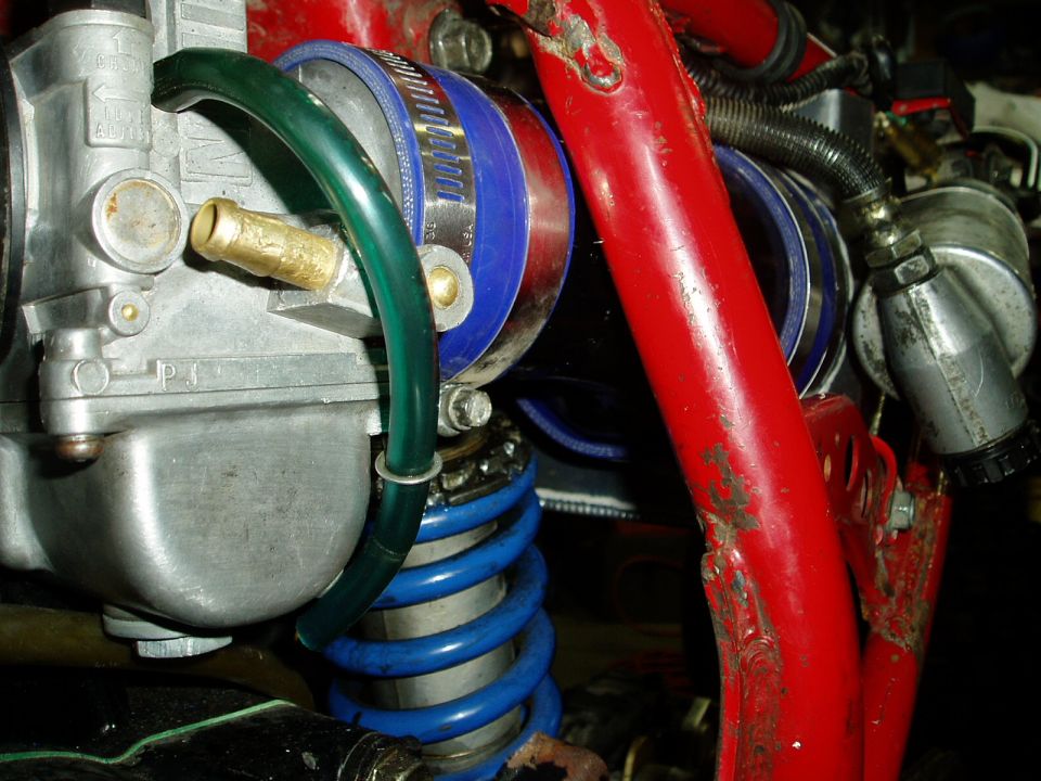 Close-up of a carburetor with blue coilover suspension and red frame