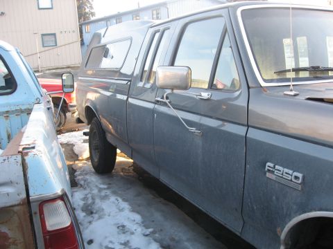 1990 Ford F-250 - A gray Ford F-250 pickup truck with a camper shell is parked in a lot with snow on the ground.