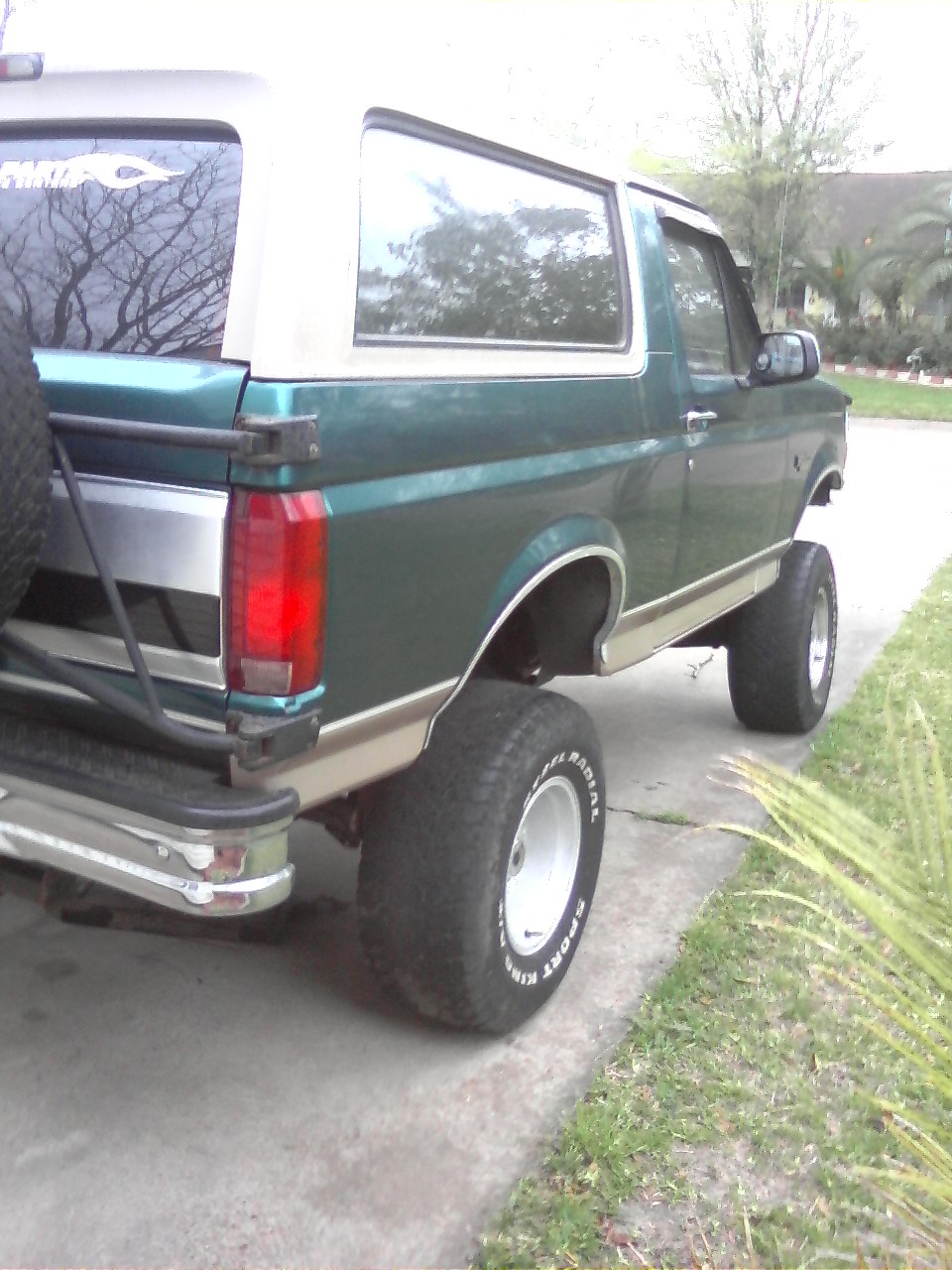 1996 Ford Bronco, green and tan, lifted with large tires, spare tire mounted on rear door