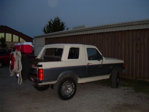 1991 Ford Bronco - A two-tone Ford Bronco is parked outside a building with a wooden fence.