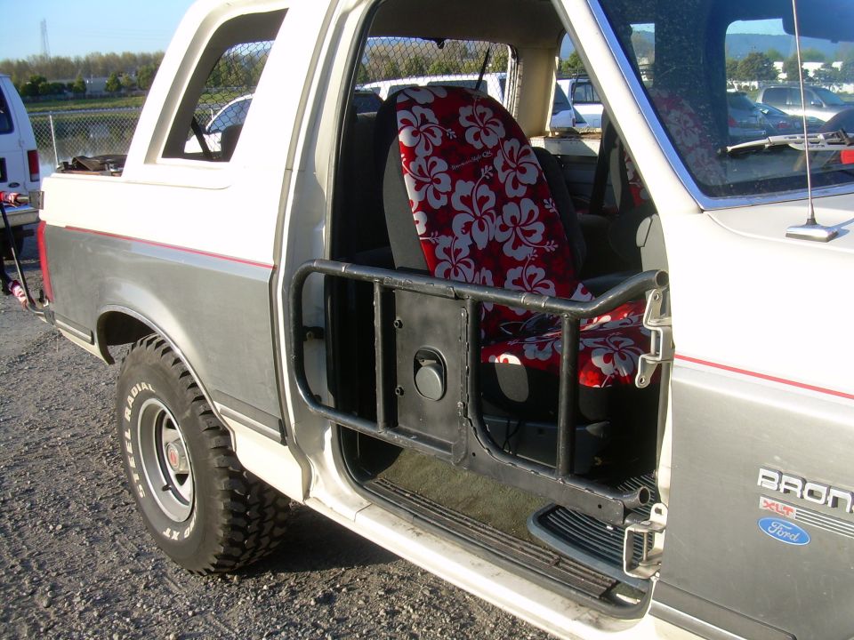 Side view of a 1991 Ford Bronco showing the interior with Hawaiian print seat covers and a roll cage