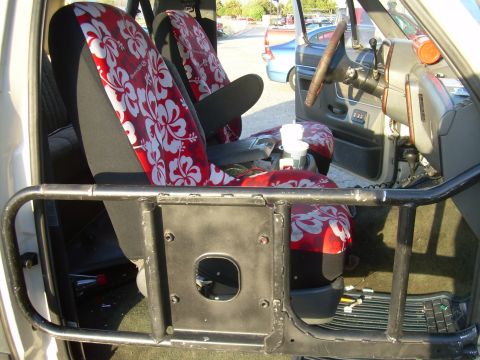 1991 Ford Bronco - The interior of a vehicle shows custom seat covers and a roll cage, with a view of the steering wheel and dashboard.