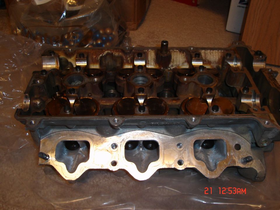Engine cylinder head with valves and camshafts visible. Some oil residue is present