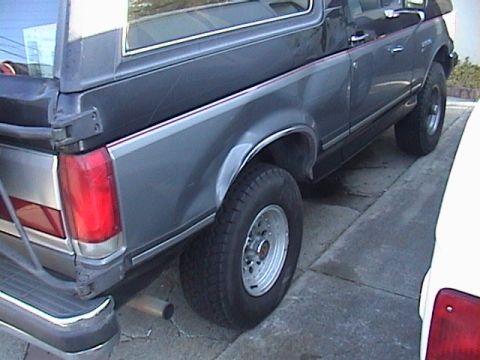 1990 Ford Bronco - This dark gray SUV shows its rear quarter panel and side profile, chrome trim and silver wheels.