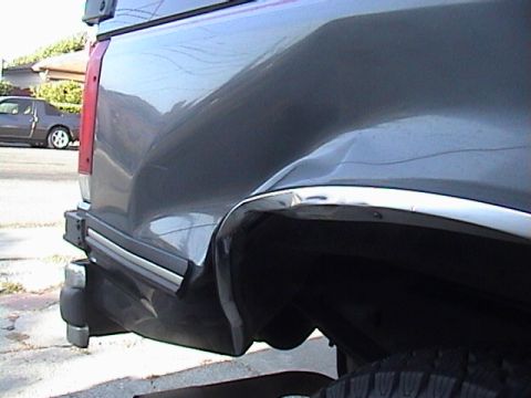 1990 Ford Bronco - Damage to the rear quarter panel of a gray truck, with another vehicle in the background.