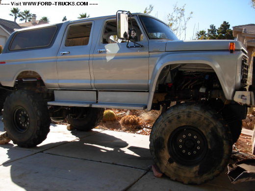Silver lifted Ford truck on huge mud tires, side view in driveway