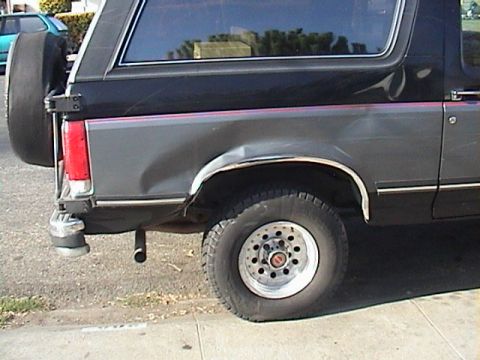 1990 Ford Bronco - Rear driver side of a 1990 Ford Bronco shows damage and a flat tire.
