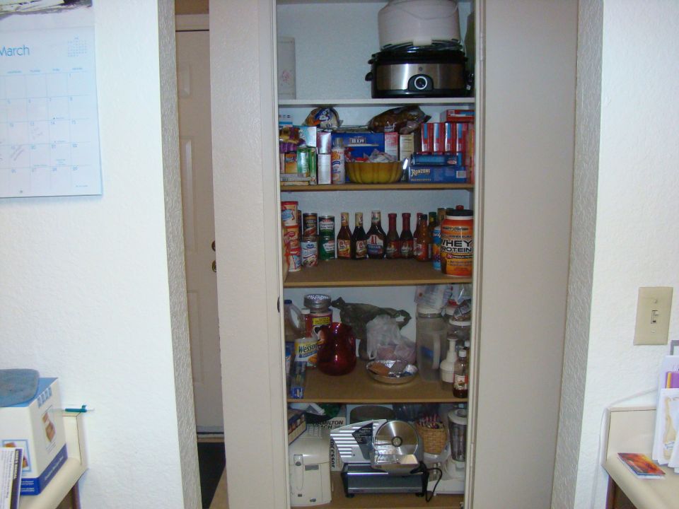 Pantry shelves stocked with canned goods, bottles, boxes, and appliances like a food slicer