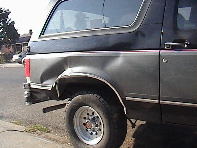 Dark gray Ford Bronco with significant rear quarter panel damage, seen from the side