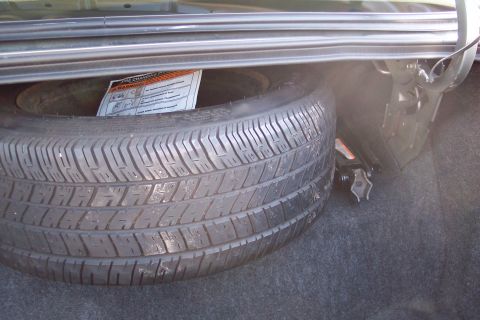 2001 Ford Crown Victoria - The trunk of a car contains a spare tire and a jack, along with a tire changing instruction manual.