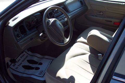 2001 Ford Crown Victoria - The interior of a car, the dashboard, steering wheel, and tan seats. A floor mat with footprints is visible.