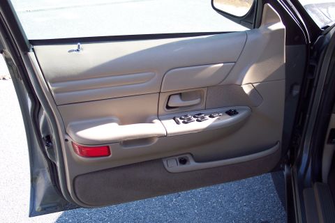 2001 Ford Crown Victoria - The interior door panel of a car shows power window controls and a red reflector near the bottom.