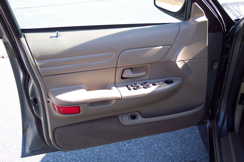 Driver's side door interior with tan trim, power window controls, and a red reflector
