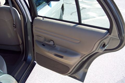 2001 Ford Crown Victoria - Interior view of a car's rear passenger door, revealing the tan door panel and seat upholstery.