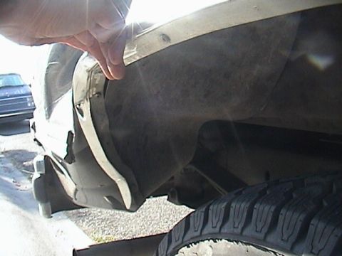 1990 Ford Bronco - Close-up view of a vehicle's wheel well and tire, with a hand touching the fender trim.
