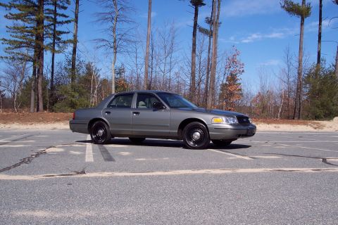 2001 Ford Crown Victoria - A gray 2001 Ford Crown Victoria is parked in an outdoor lot with trees in the background under a blue sky.