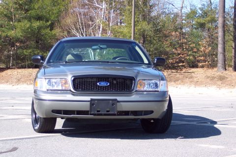 2001 Ford Crown Victoria - A 2001 Ford Crown Victoria is shown from the front, parked in an outdoor lot with trees in the background.