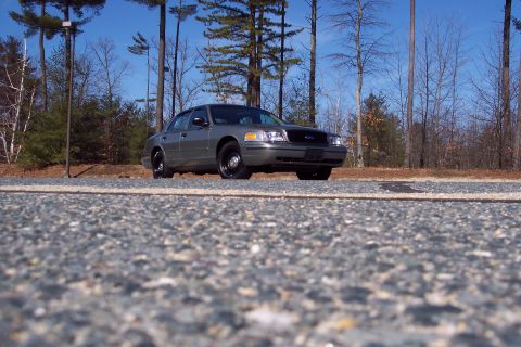 2001 Ford Crown Victoria - A gray 2001 Ford Crown Victoria is parked on the side of a road with trees in the background.