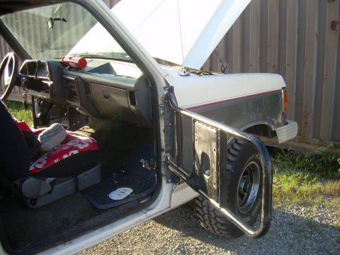 1991 Ford Bronco - Interior view of a 1991 Ford Bronco, showing the dashboard and driver's seat, with the door open to reveal a custom spare tire carrier.