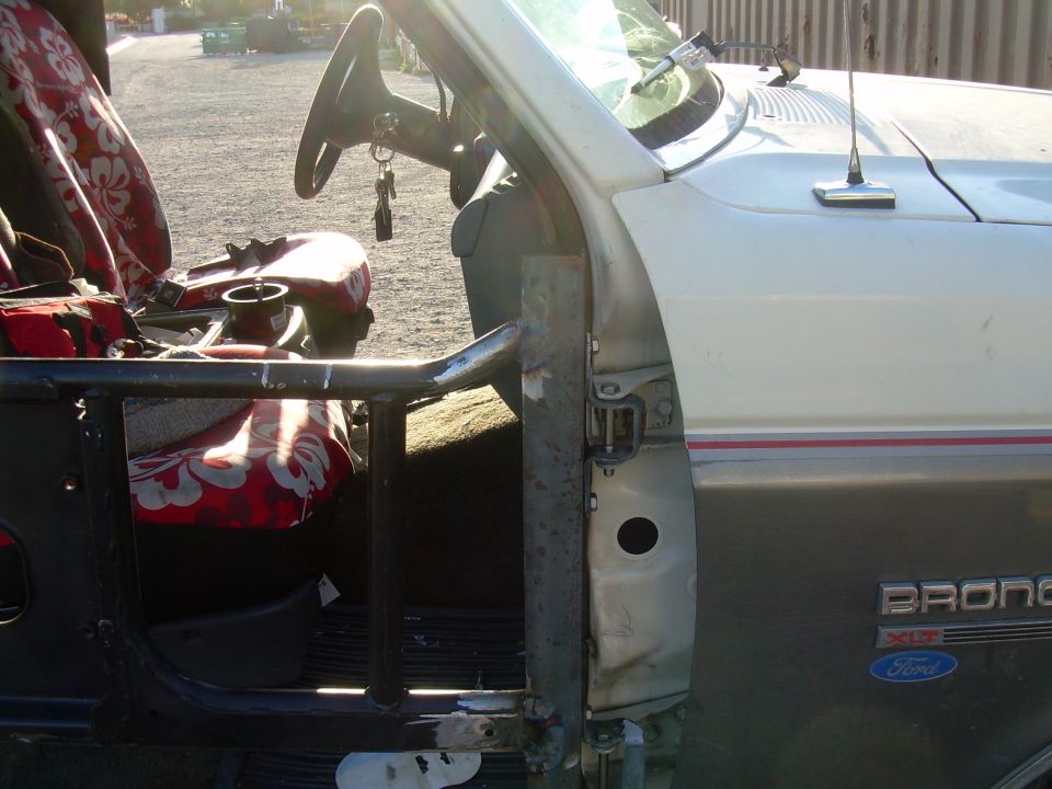 Interior of a 1991 Ford Bronco, showing the driver's seat, steering wheel, and door frame with a roll cage installed