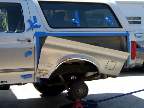 1996 Ford Bronco - White and silver two-tone Ford Bronco SUV viewed from the rear passenger side, elevated on a floor jack with the rear wheel off the ground.…