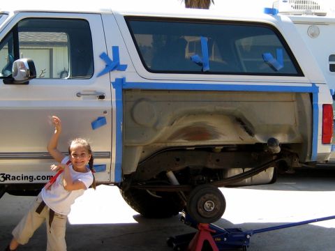 1996 Ford Bronco - A white two-door Ford Bronco SUV in mid-restoration, with blue painter's tape masking the windows and body seams and the rear quarter panel…
