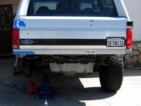 1996 Ford Bronco - Rear view of a white Ford Bronco with a black lower tailgate stripe, Ford oval logo, and California plate '5FTN174', lifted on oversized mu…