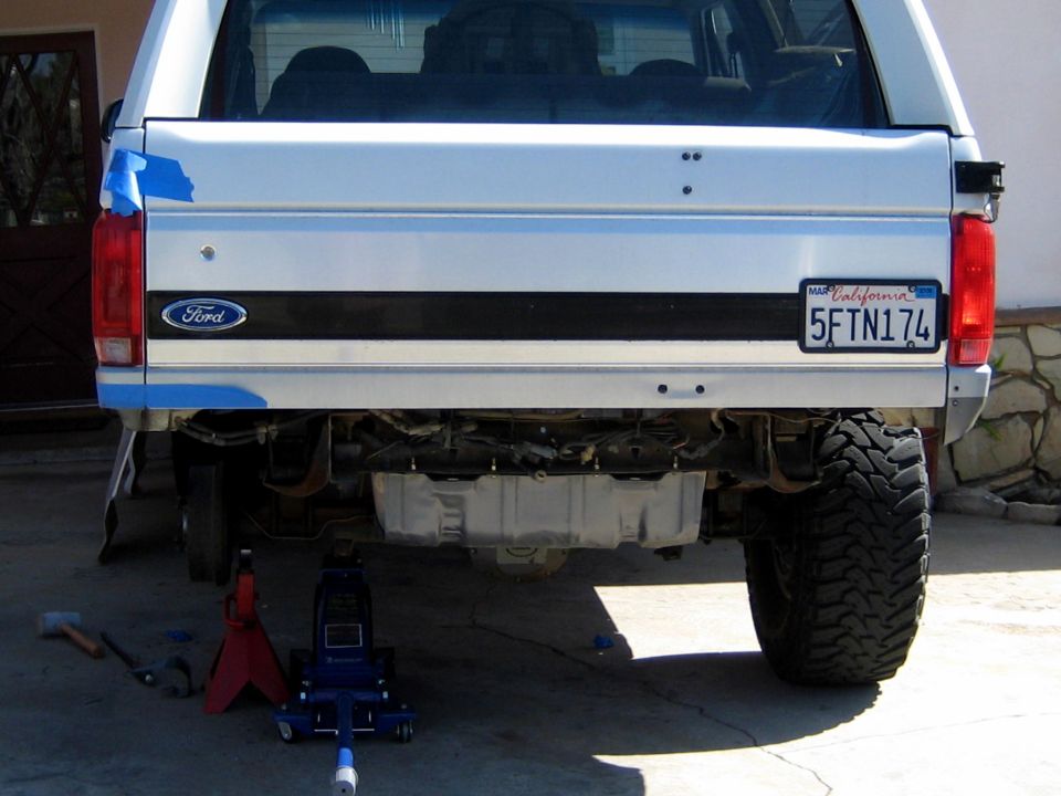 Rear of white Ford Bronco lifted on floor jack and jack stand, oversized tires